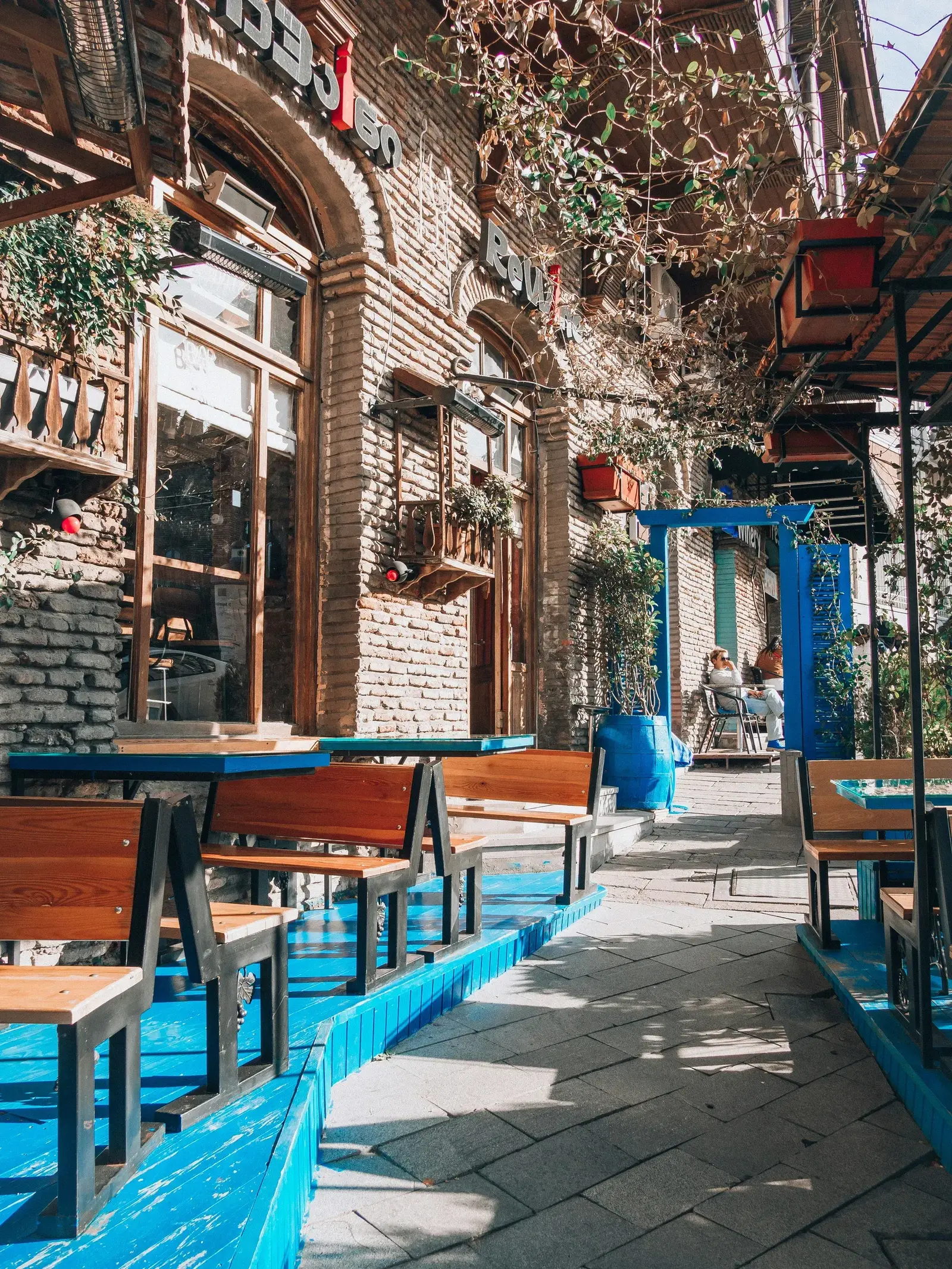 A cozy outdoor café with blue-painted wooden furniture and trailing vines in Tbilisi