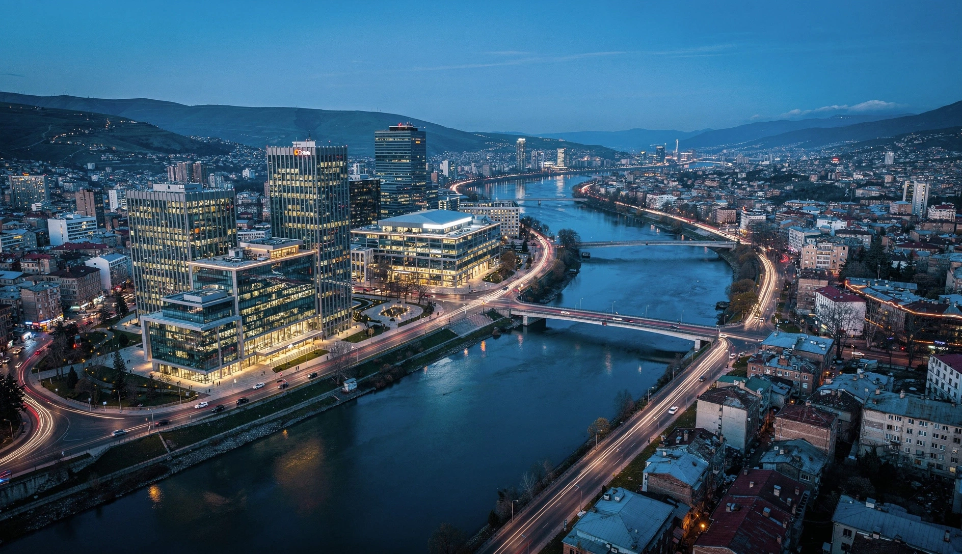 Aerial view of modern Tbilisi cityscape with glass buildings and the Kura River at blue hour