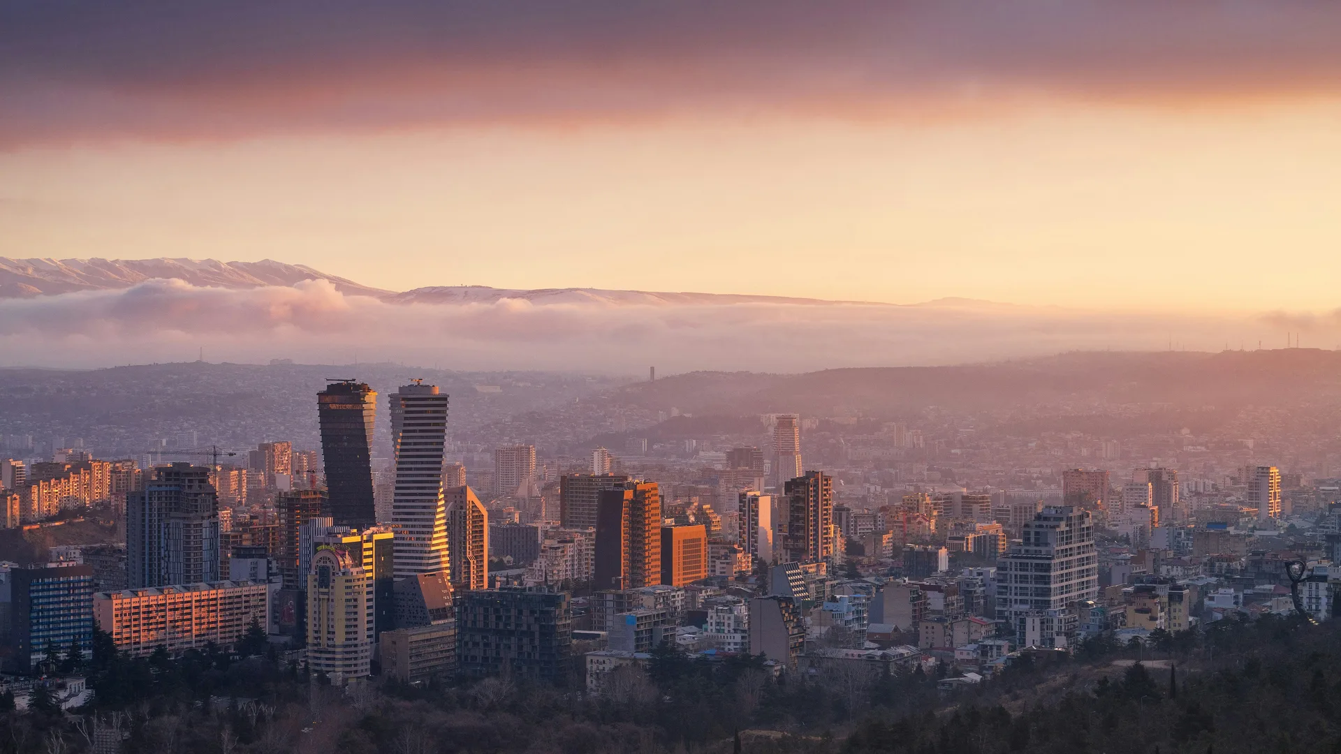 Panoramic view of Tbilisi's Vake district at sunset with modern high-rises and mountains in the background