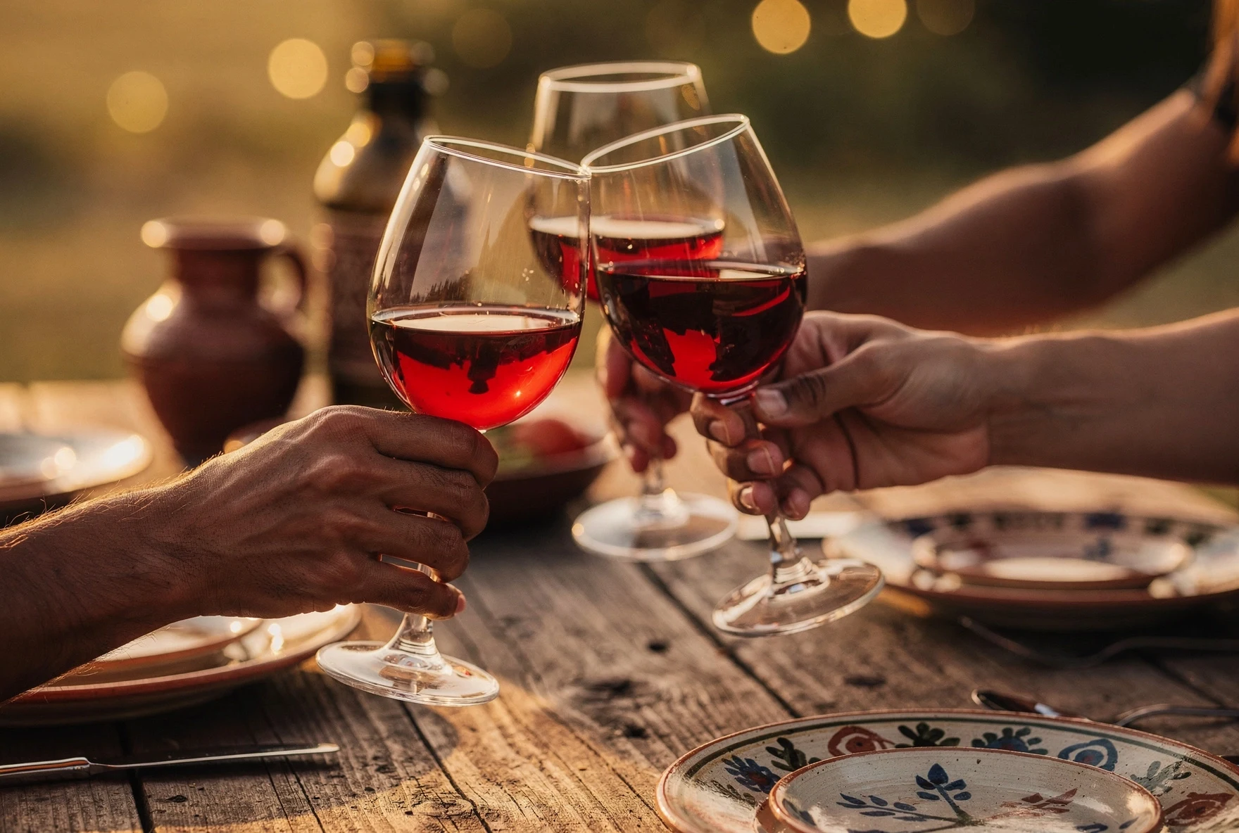 Friends clinking wine glasses at a Georgian dinner table with ceramic jugs in warm evening light